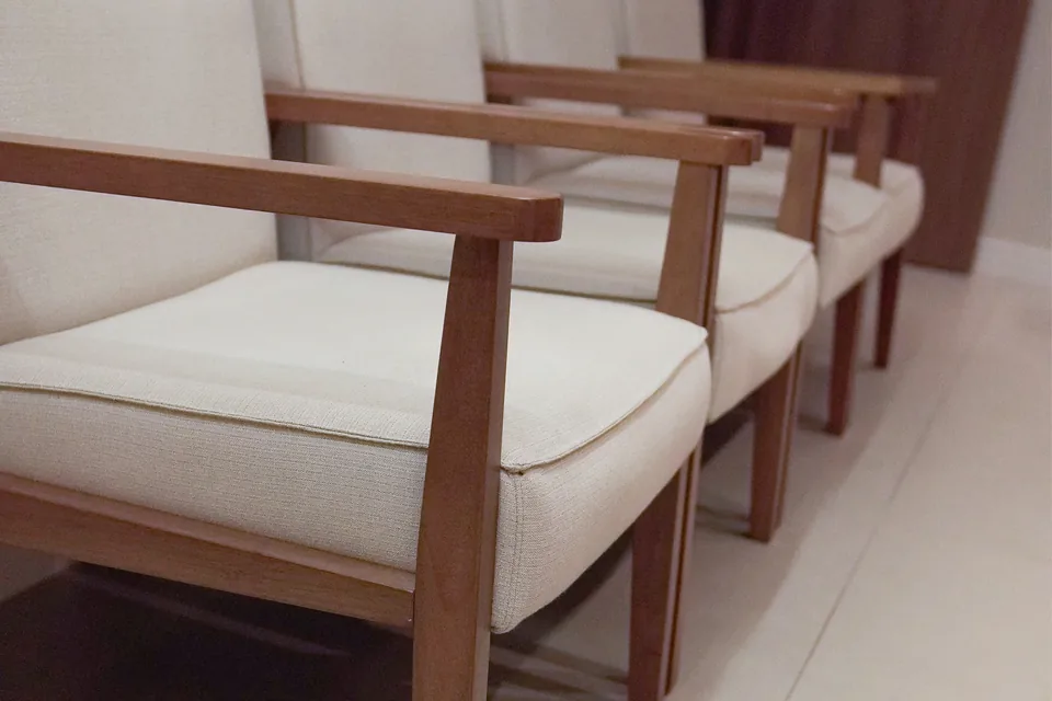 Poltronas claras de madeira em fila na recepção.