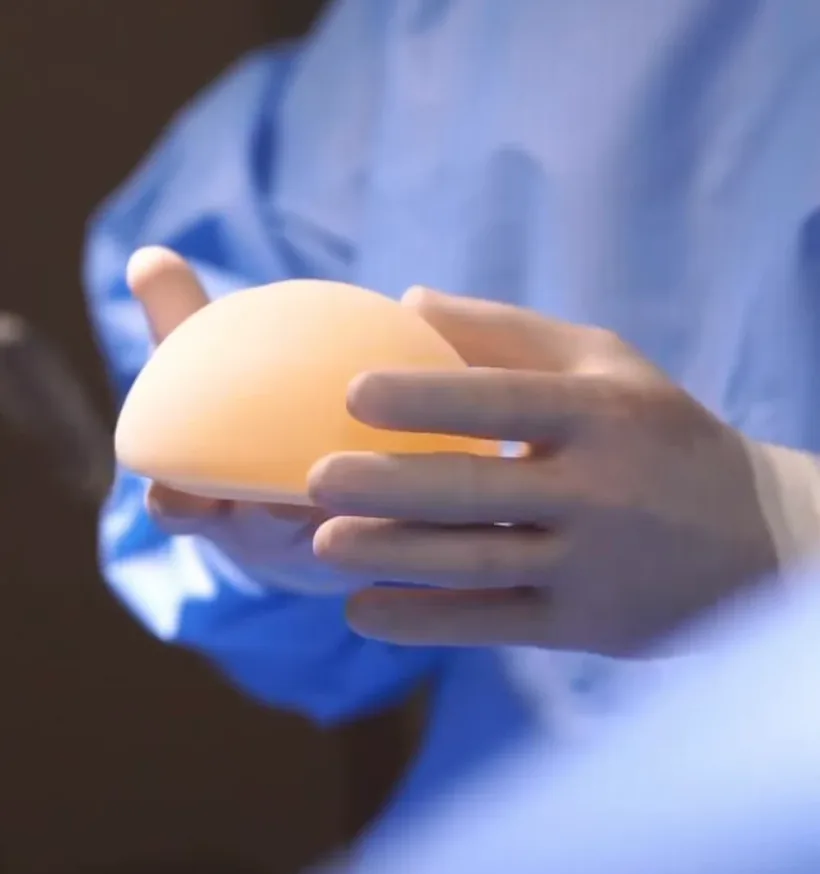 Mãos de luva segurando uma prótese de silicone, no centro cirúrgico.